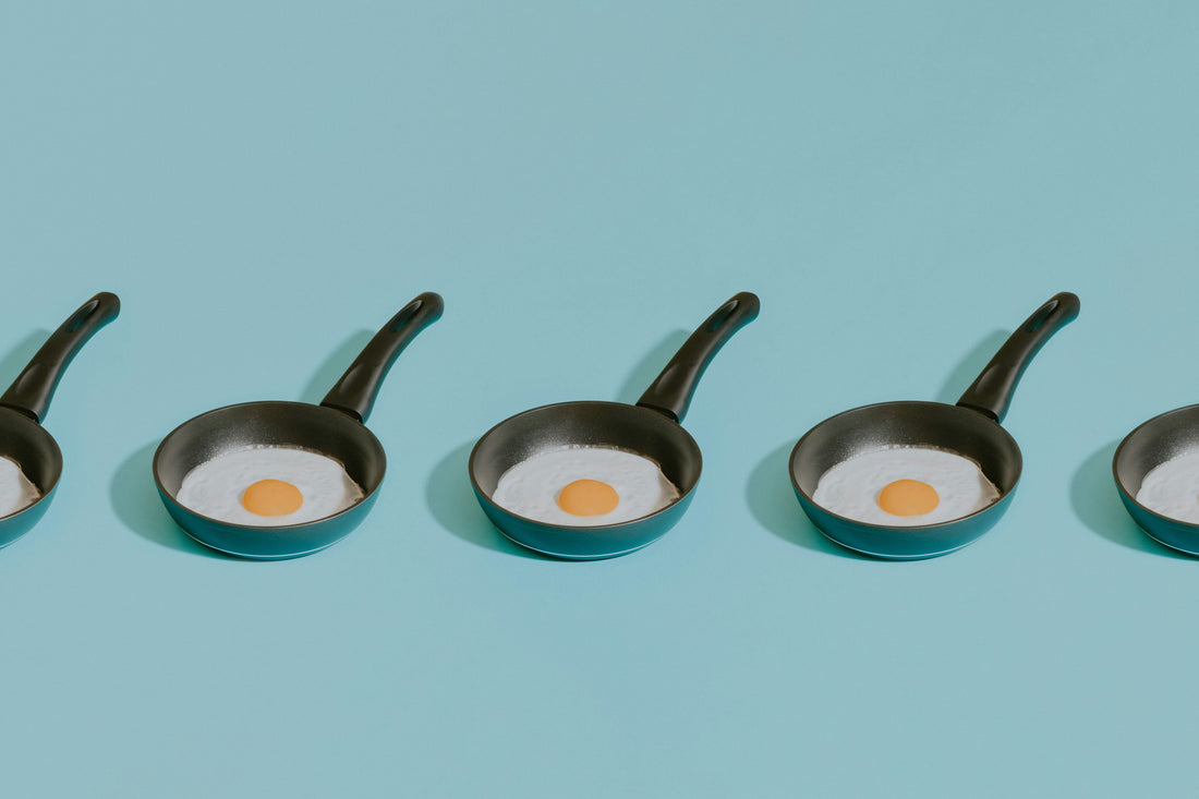 Four frying pans on a table, one holding a fried egg