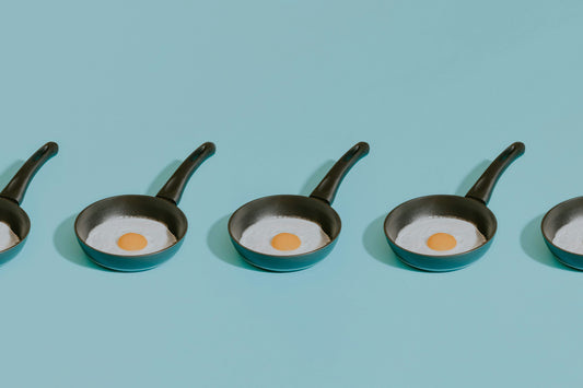 Four frying pans on a table, one holding a fried egg